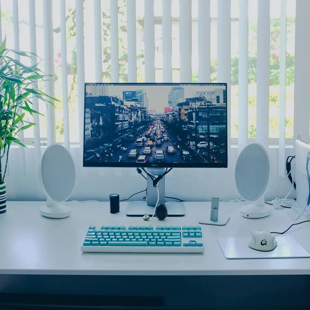 Poste de travail avec écran, clavier et enceintes sur un bureau blanc
